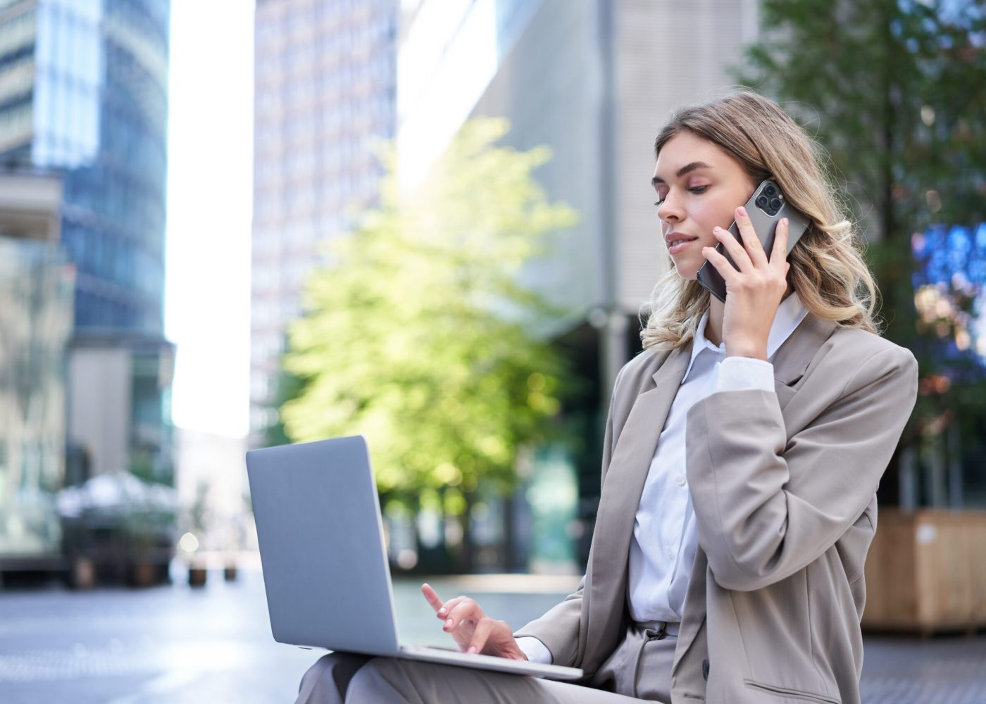 Businesswoman checking diagram and work on laptop, calling someone on mobile phone, sitting outdoors in city centre.