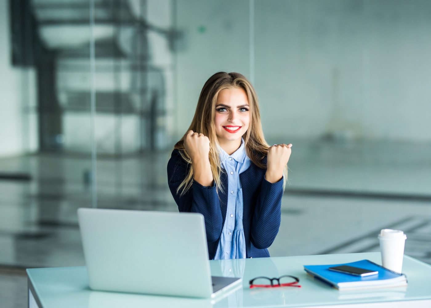 Excited businesswoman winning after achievement reading a smart phone sitting in a desktop at office