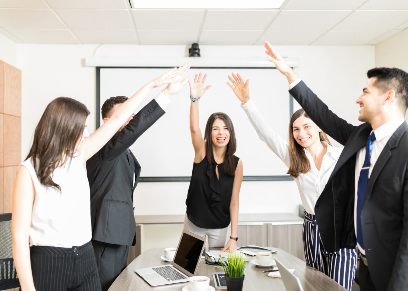 Happy multiethnic businessmen and businesswomen raising hands to celebrate in boardroom