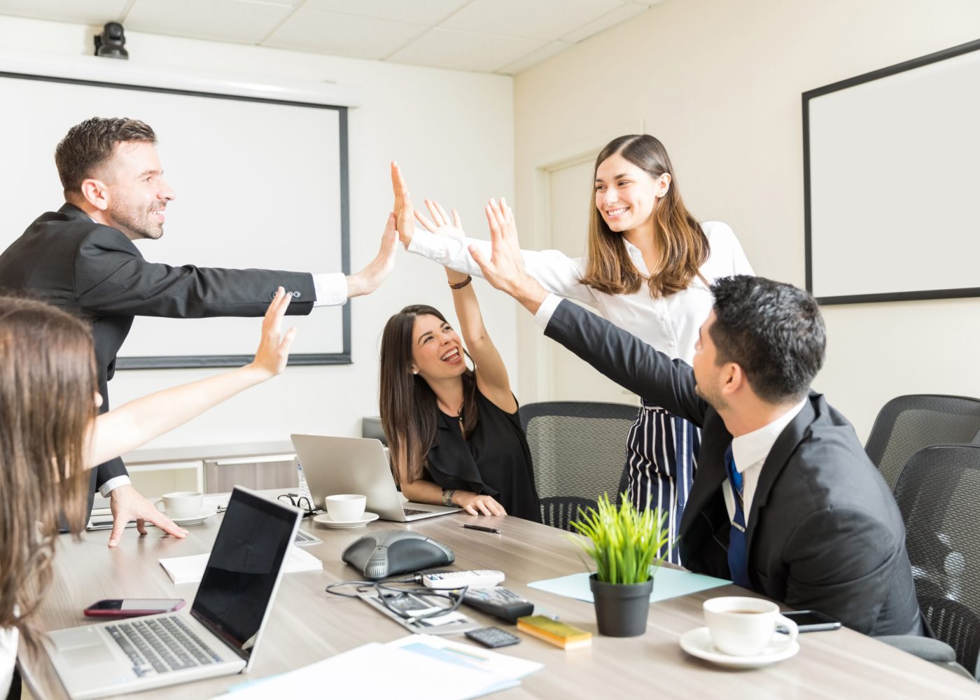 Happy subordinates giving high-five after successfully undertaking new project in boardroom