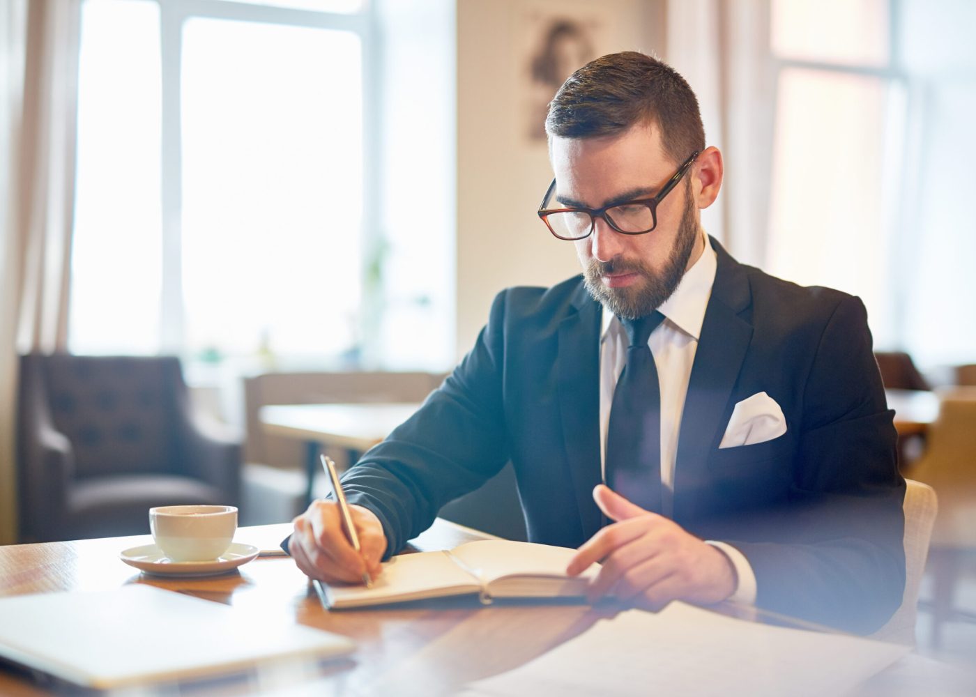 Busy director or ceo in suit sitting by table in cafe and writing in notebook