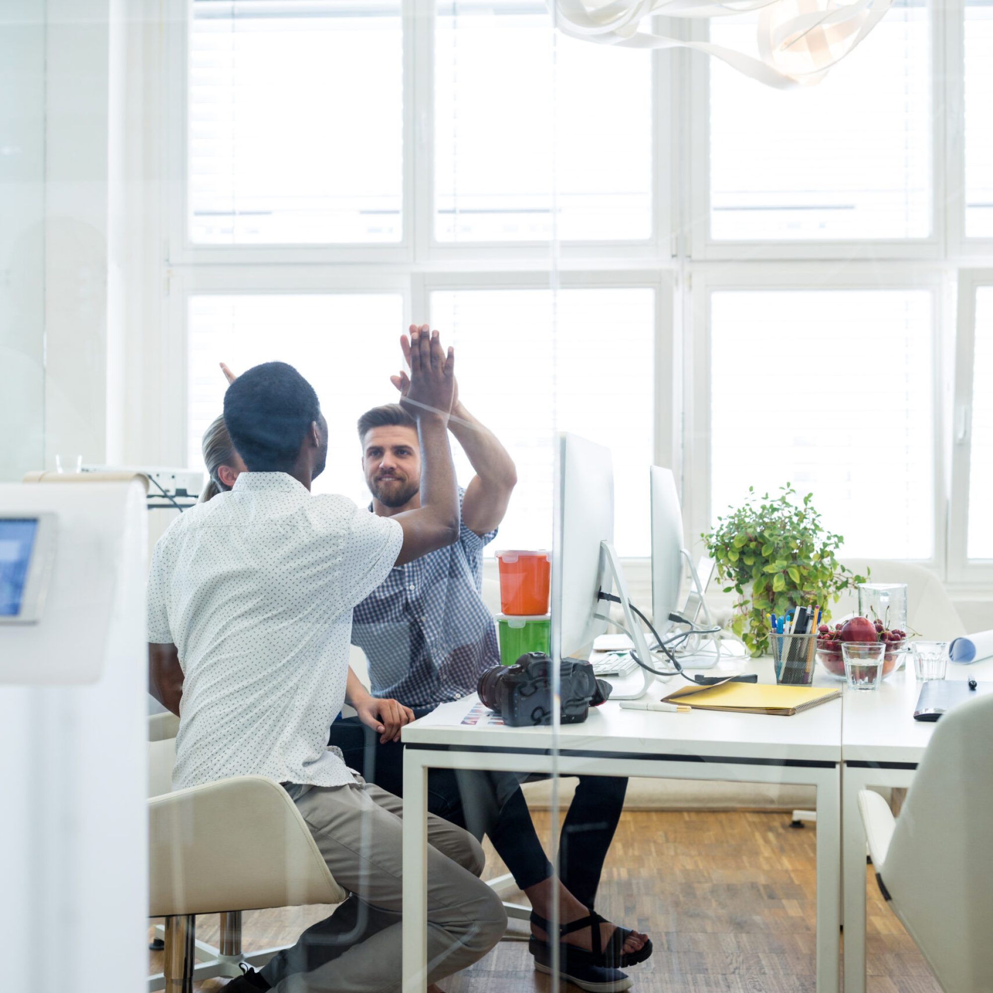 Two male graphic designers giving high five to each other in office